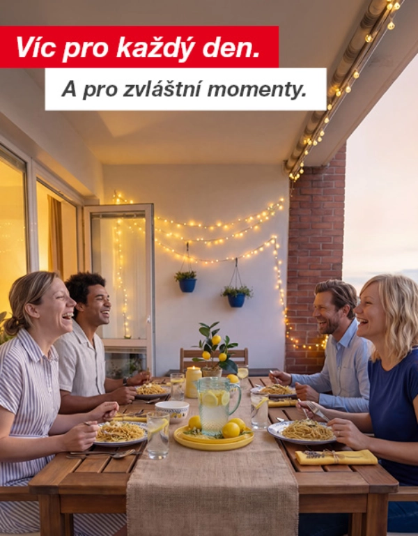 Čtyři osoby si užívají večerní jídlo s těstovinami a limonádou na ozdobeném balkoně se světelnými řetězy a květinami v květináčích.
