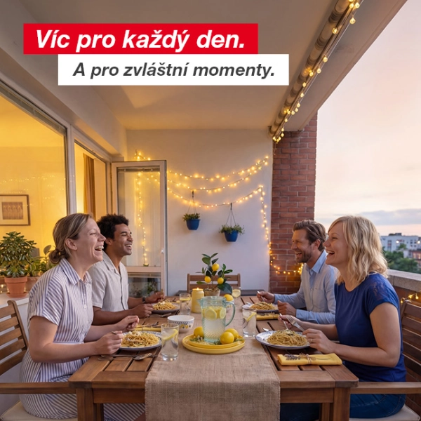 Čtyři osoby si užívají večerní jídlo s těstovinami a limonádou na ozdobeném balkoně se světelnými řetězy a květinami v květináčích.