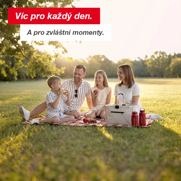 Čtyřčlenná rodina si užívá piknik na dece ve slunném parku se stromy a otevřenou travnatou plochou.