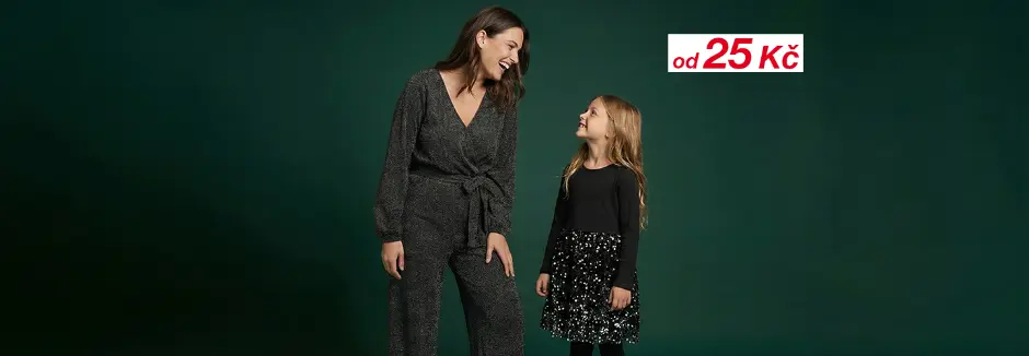 Žena ve stylovém šedém kombinézu stojí vedle dívky v černém topu a sukni s flitry, obě na tmavě zeleném pozadí.