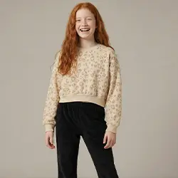 Dívka v béžovém svetru a černých kalhotách před světlým pozadím.