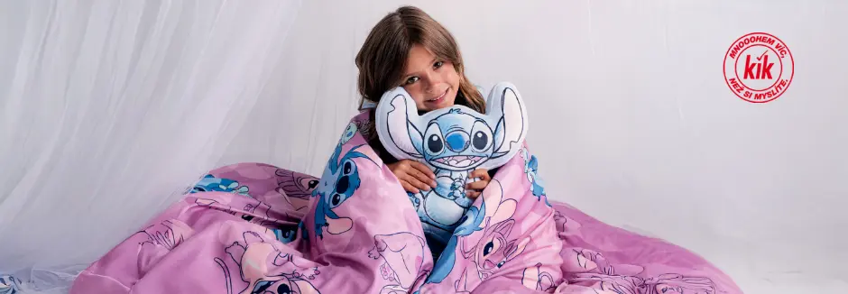 Dítě je zabalené do růžové deky s motivem Stitch, drží plyšového Stitch a sedí na měkkém bílém pozadí.