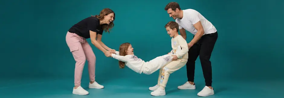 Čtyřčlenná rodina sedí společně na pohovce a usmívá se, se měkkými polštáři a útulným obývacím pokojem v pozadí.