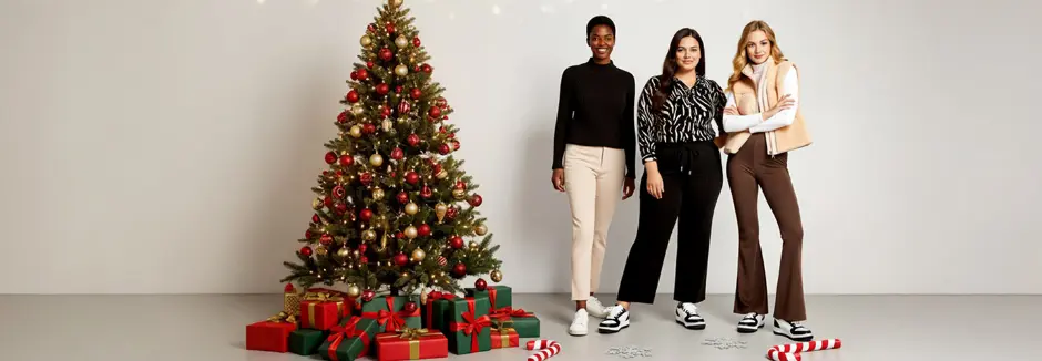 Tři ženy pózují společně u krásně nazdobeného vánočního stromku s dárky a vytvářejí tak sváteční atmosféru.