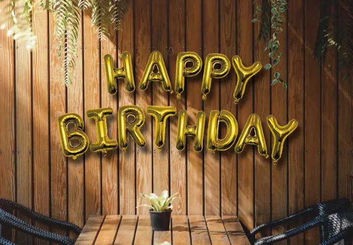Zlaté balónky s nápisem „Happy Birthday“ na dřevěné stěně.