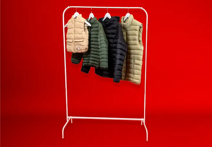 Bílý stojan na oblečení zobrazuje čtyři prošívané vesty v různých barvách – béžové, tmavě zelené, námořnické modré a olivové – na červeném pozadí.
