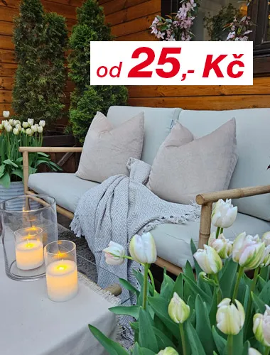 Černý gril na dřevěné uhlí stojí vedle dřevěného jídelního stolu připraveného k večeři, se svíčkami a židlemi, zasazeného do zeleného venkovního prostředí.