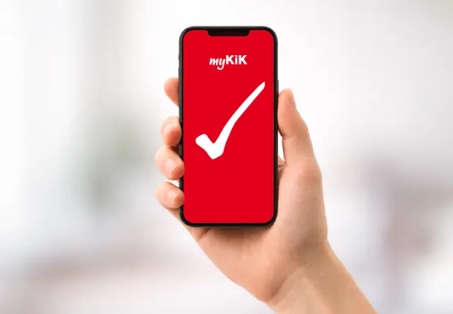 Osoba drží smartphone s aplikací myKiK, která má červené pozadí s bílým zaškrtnutím.