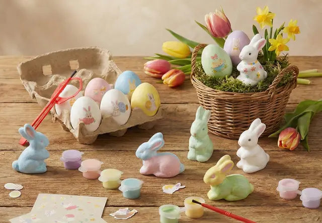 Barevní papíroví zajíčci a růžový keramický zajíc mezi rozkvetlými květinami a dekorativními vázami v živé jarní zahradě.