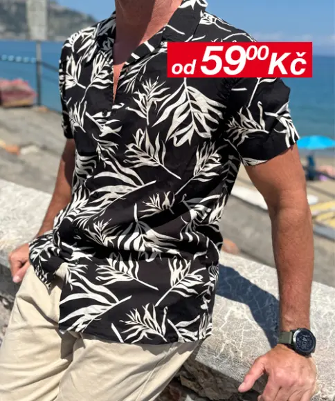 Muž v ležérní póze, oblečený do zeleného trička a světle modrých šortek, s černými sportovními botami, před jemným pozadím.