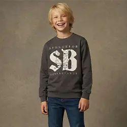 Chlapec v šedé mikině a džínách se usmívá před neutrálním pozadím.