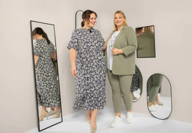 Zwei Frauen stehen in einer stilvollen Umgebung mit Spiegeln und präsentieren ein geblümtes Kleid und ein schickes grünes Outfit, das Selbstbewusstsein und Eleganz ausstrahlt. Zwei Frauen stehen in einer stilvollen Umgebung mit Spiegeln und präsentieren ein geblümtes Kleid und ein schickes grünes Outfit, das Selbstbewusstsein und Eleganz ausstrahlt.