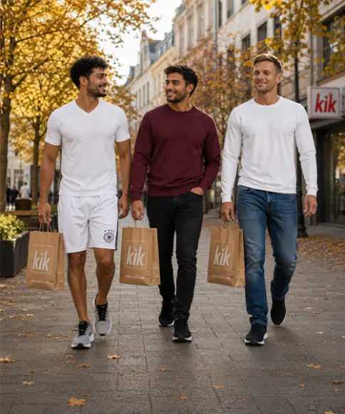 Tři muži ve sportovních a podzimních volnočasových outfitech s nákupními taškami KiK při procházce městem