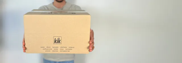Osoba drží velkou kartonovou krabici s logem „Kik“, na jejíž straně jsou vícejazyčná poděkování.