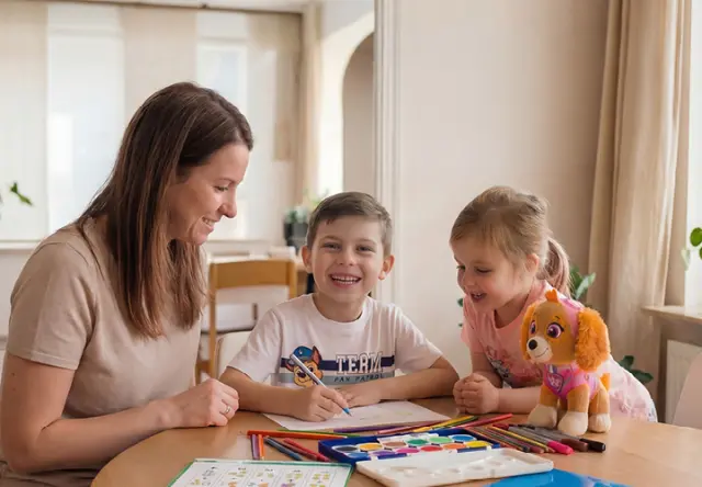 Žena maluje společně se dvěma dětmi u stolu. Pastelky, vodové barvy a plyšák Tlapková patrola vybízejí ke kreativnímu tvoření. Žena maluje společně se dvěma dětmi u stolu. Pastelky, vodové barvy a plyšák Tlapková patrola vybízejí ke kreativnímu tvoření.