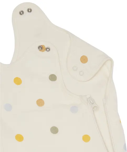 Detail krémově zbarveného dětského oděvu s barevnými puntíky, patentními knoflíčky a bočním zipem.