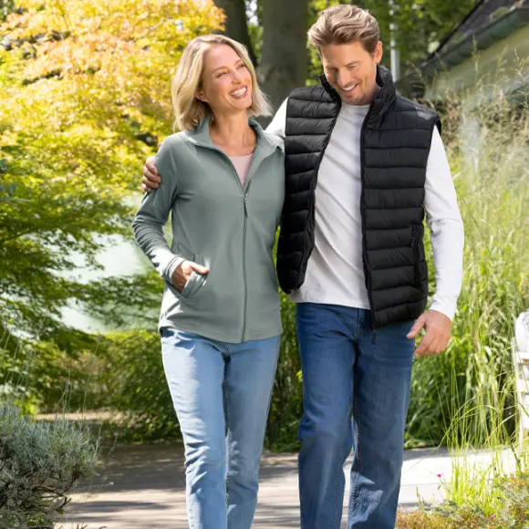 Pár si užívá procházku venku, obklopený zelení a stromy, oba oblečeni pohodlně a ležérně.