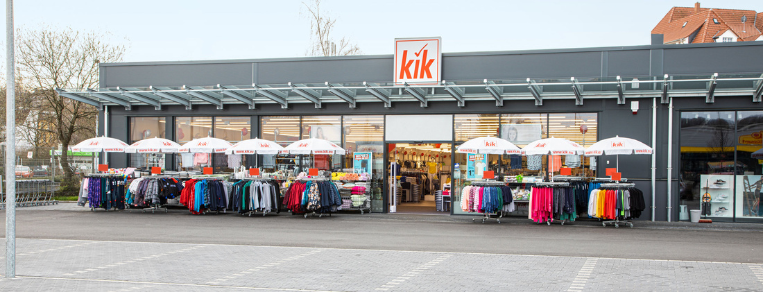 Vnější pohled na prodejnu KiK s logem KiK na dveřích a stojany s oblečením před vchodem